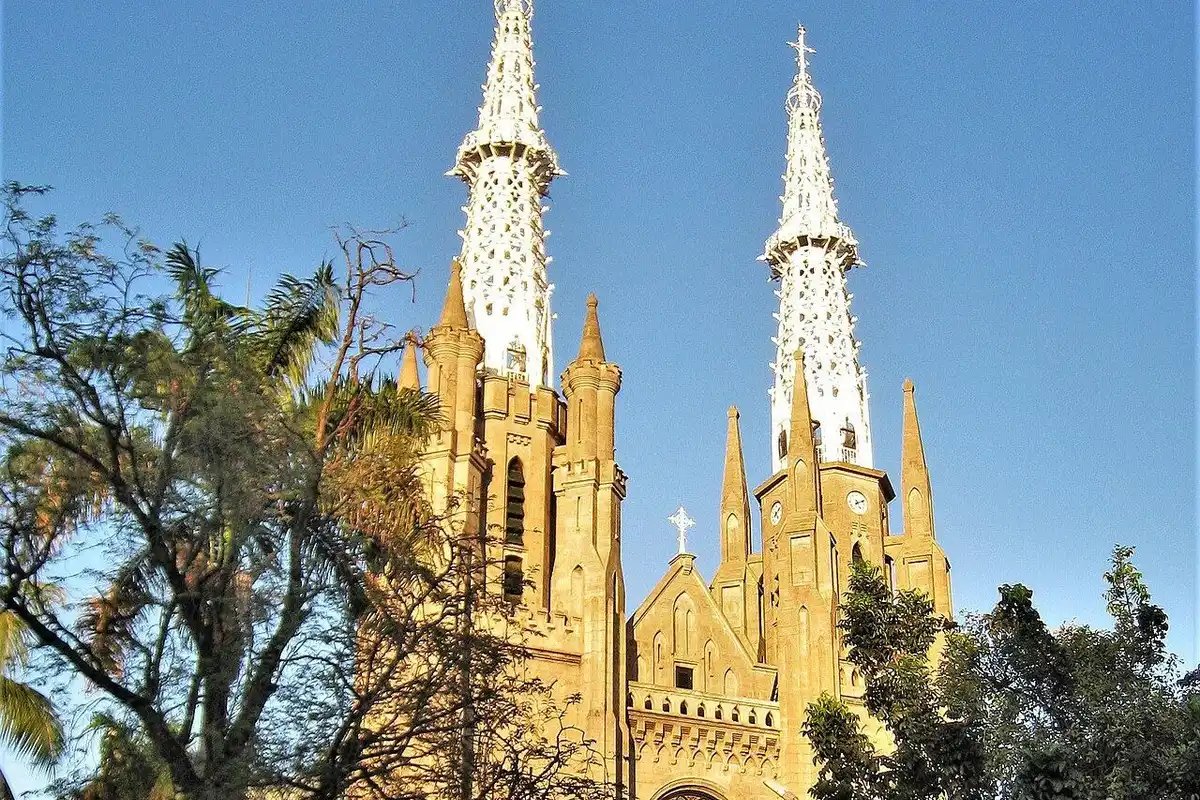 The Neo-Gothic facade and two white spires of Jakarta Cathedral in afternoon sun under a blue sky.