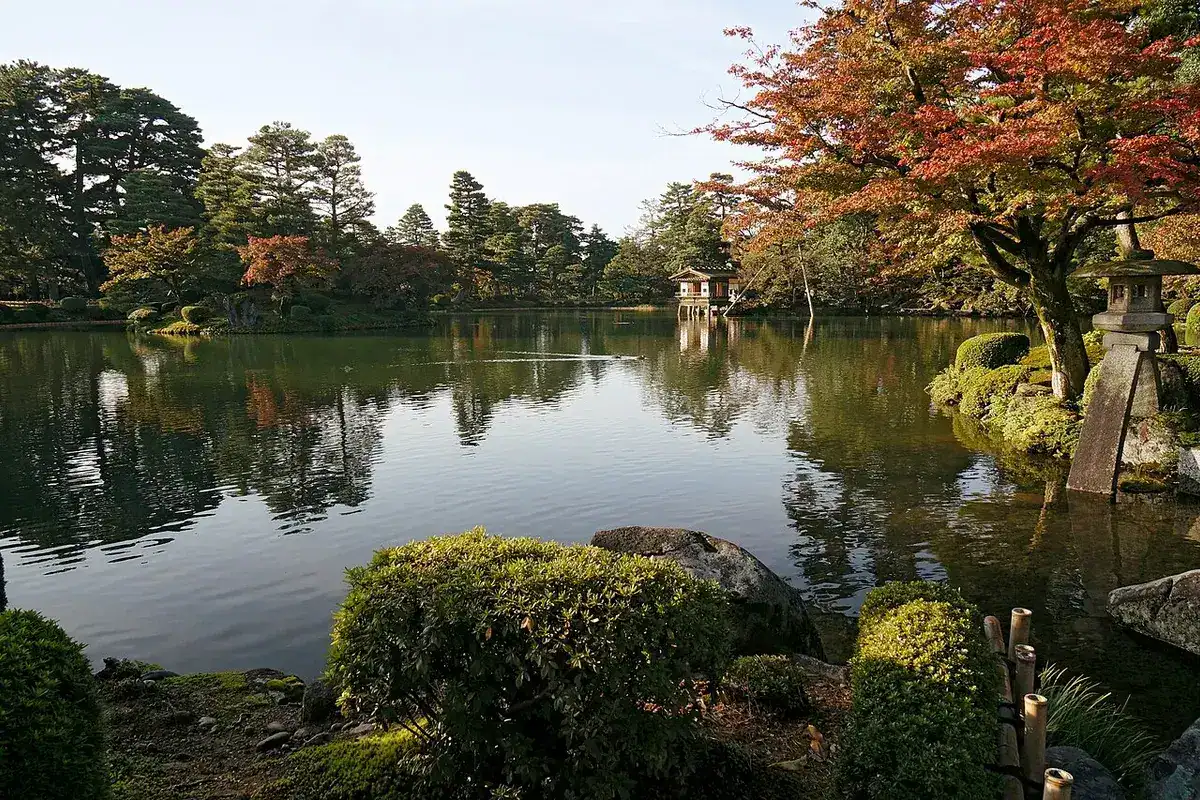 赤く色づいたカエデと石灯籠が池のほとりに並ぶ秋の兼六園。