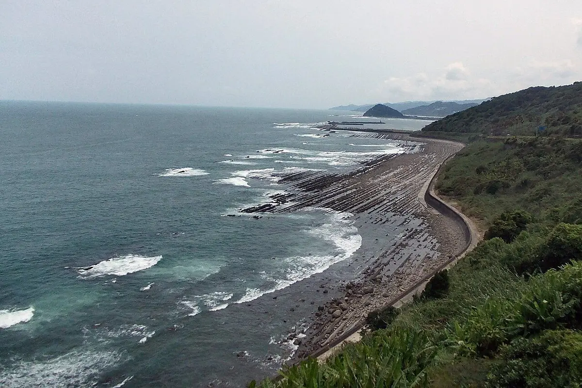 The sea, a coastline of striped rock ridges and green hills seen from the pass.