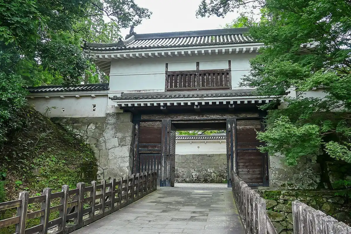 The white-walled, tile-roofed Otemon gate of Obi Castle at the end of a wooden-railed path.
