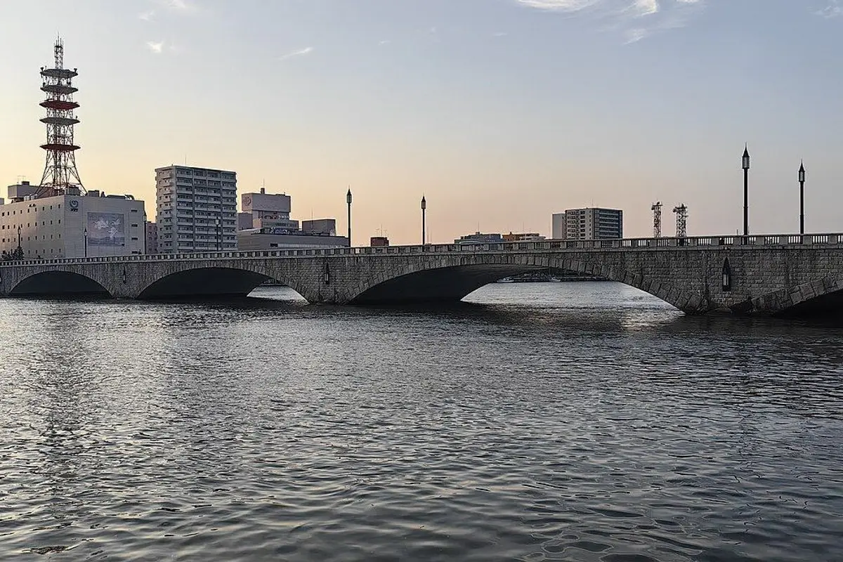 夕暮れの信濃川に架かる萬代橋の石造りのアーチと、その奥の街並み。