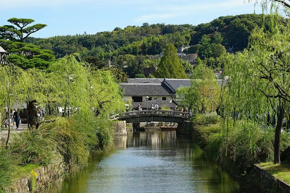 Willow-lined Kurashiki River with white-walled storehouses in the Bikan Historical Quarter.