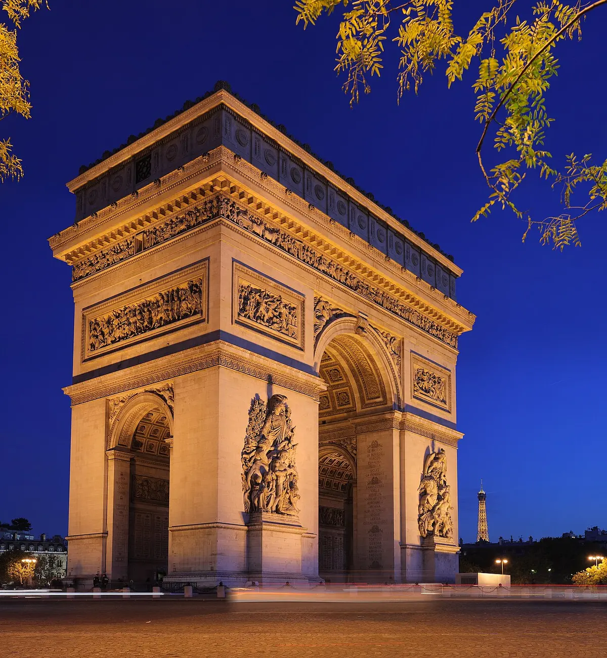 The Arc de Triomphe lit at twilight, with light trails from traffic around it