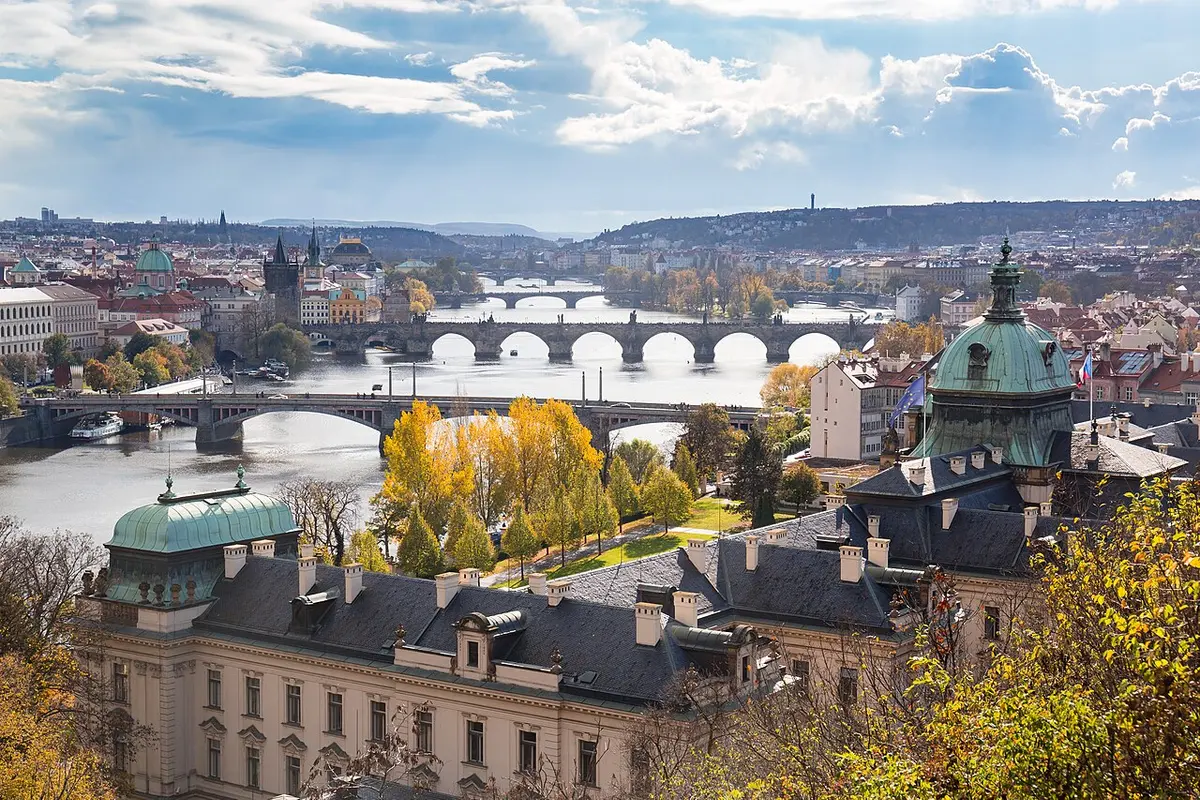 Several bridges crossing the Vltava under an autumn sky, with historic riverside buildings