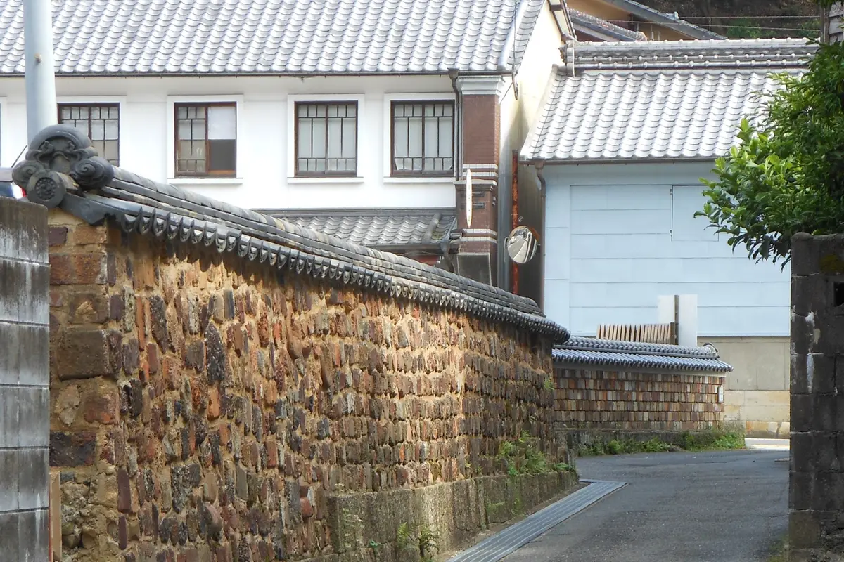 有田内山地区の細い路地に沿って、古い耐火れんがを積んだ瓦屋根の塀が続き、奥に白壁の瓦屋根の家並みが見える。