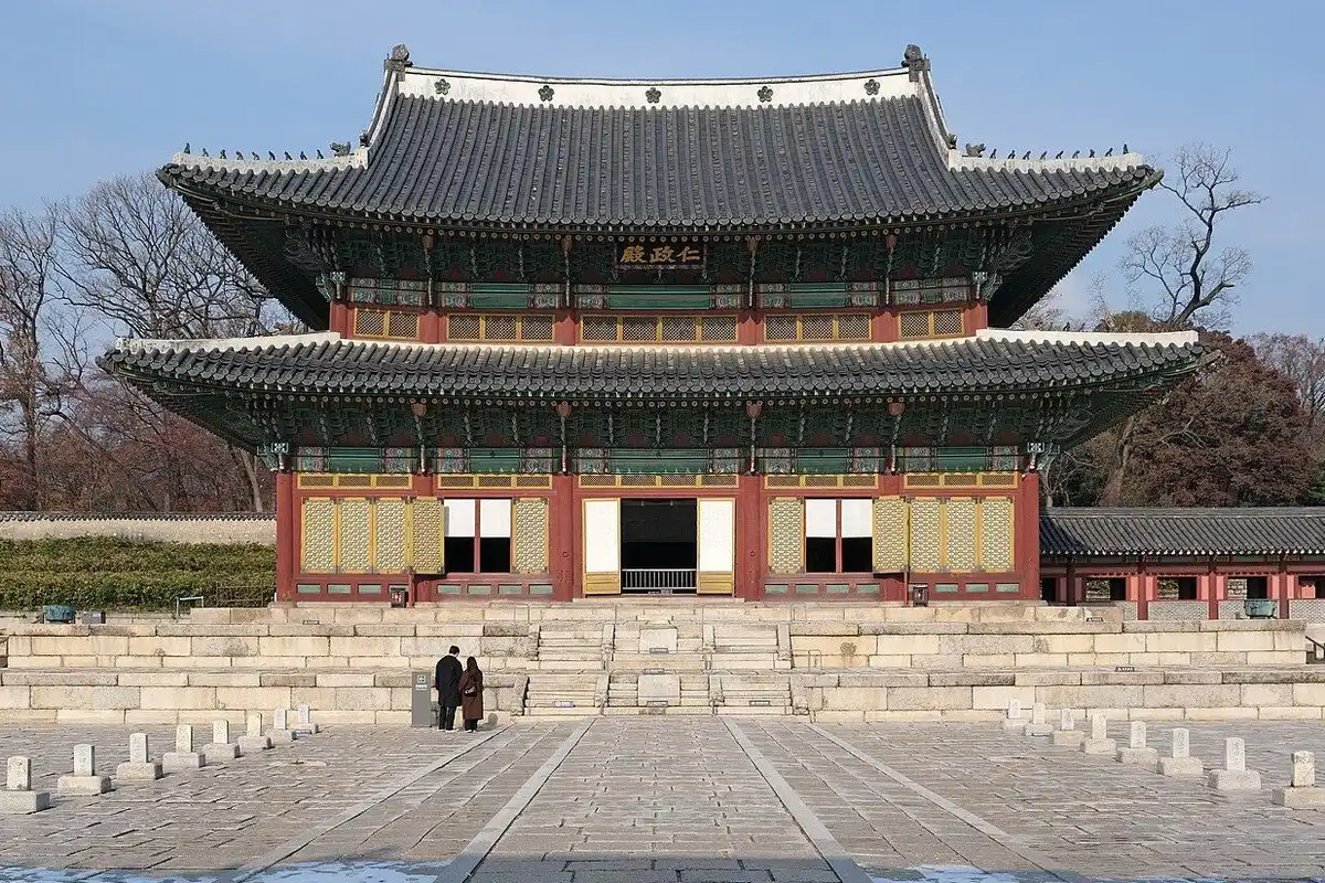 창덕궁의 정전인 인정전이 넓은 돌 마당 끝 높은 기단 위에 2층 지붕을 얹고 서 있고, 뒤로 잎이 진 늦가을 나무들이 보여요.