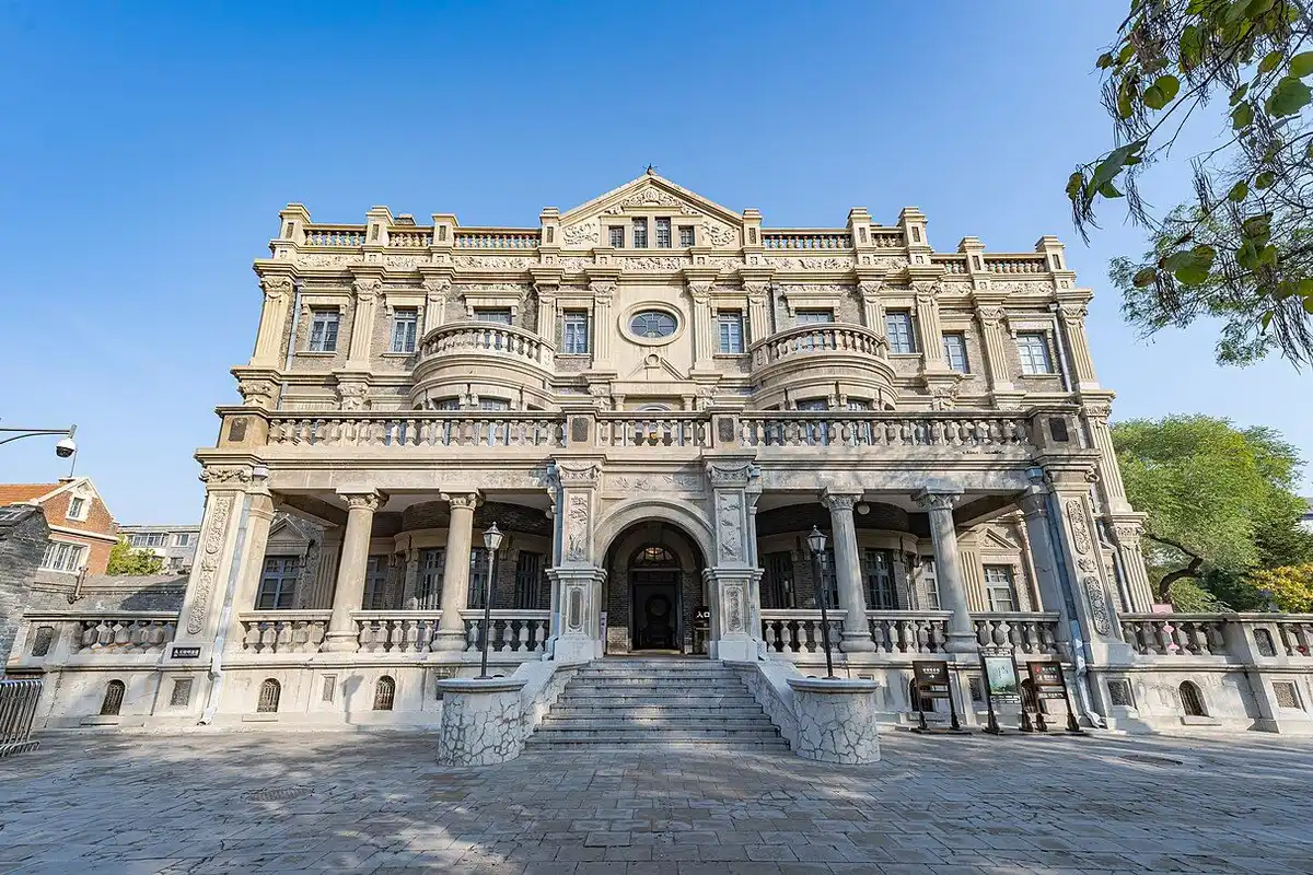 A three-storey Western-style grey stone mansion with balconies and an arched entrance under a clear sky.