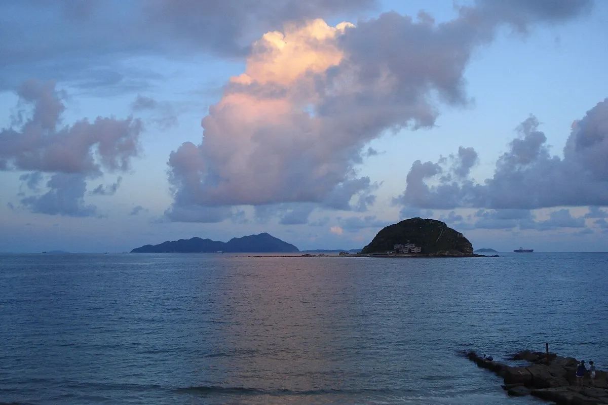 夕暮れのピンク色の雲の下、穏やかな海と小さな島が見える西涌ビーチ。