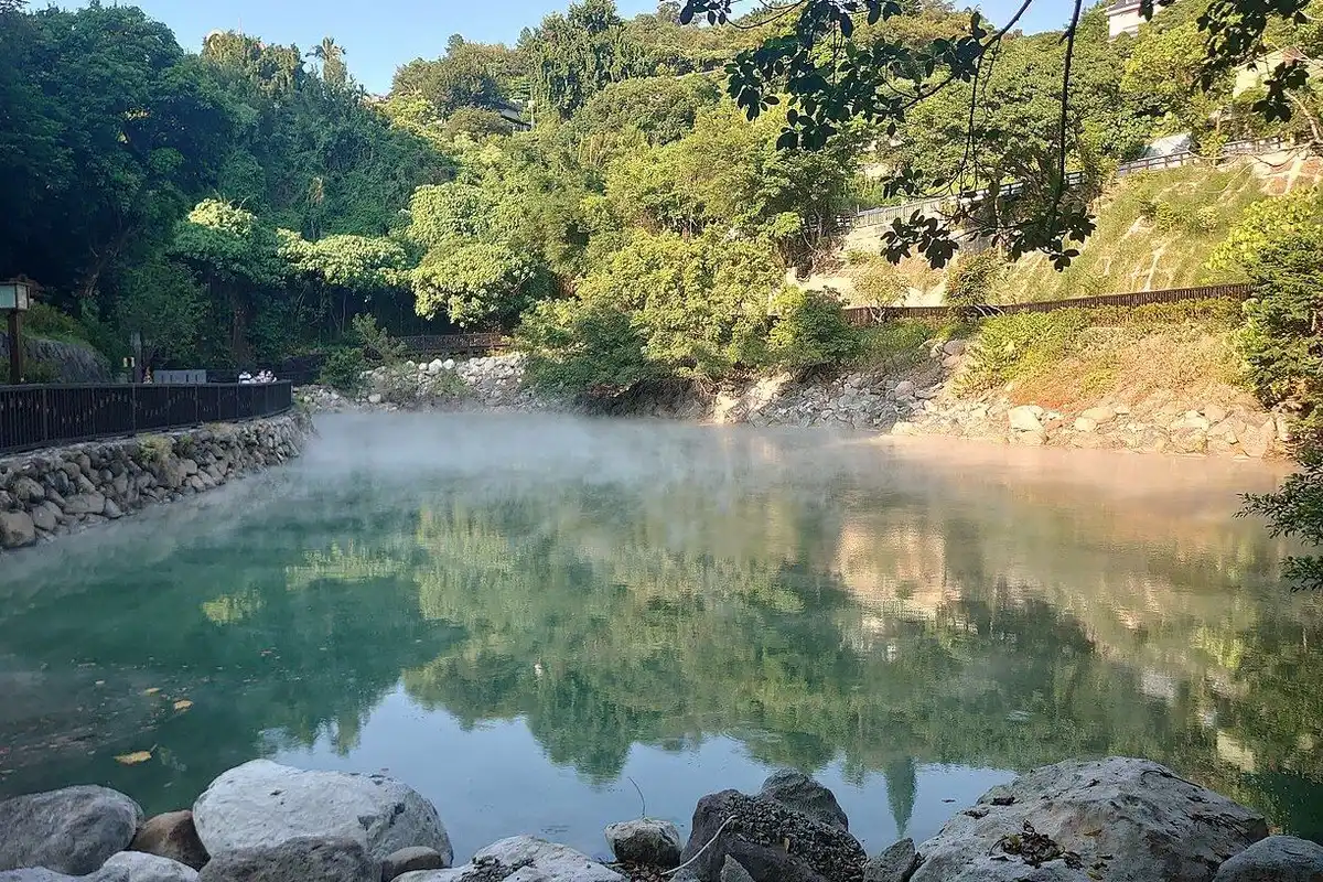 湯気が立ちのぼる翡翠色の温泉池と、水面に映る緑の木々。