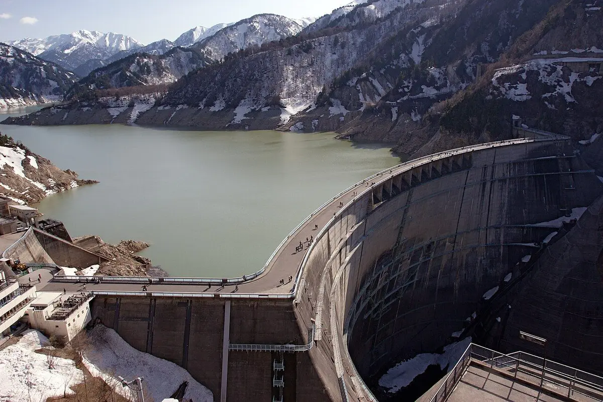 The curved Kurobe Dam and green Lake Kurobe below mountains still patched with snow.