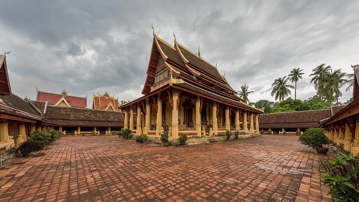 Wat Si Saket's ordination hall in its paved courtyard in Vientiane under a stormy sky.