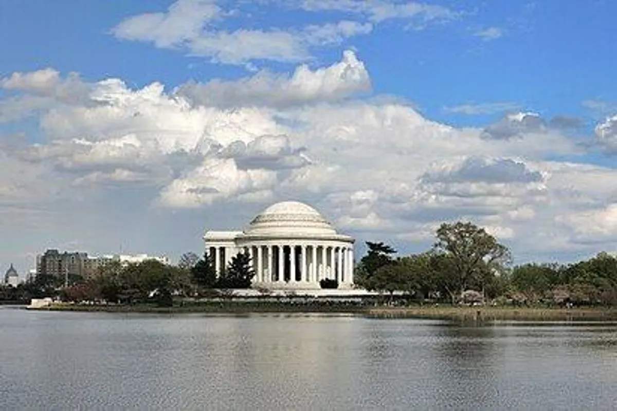 The domed Jefferson Memorial and waterside trees across the calm Tidal Basin under a blue spring sky.