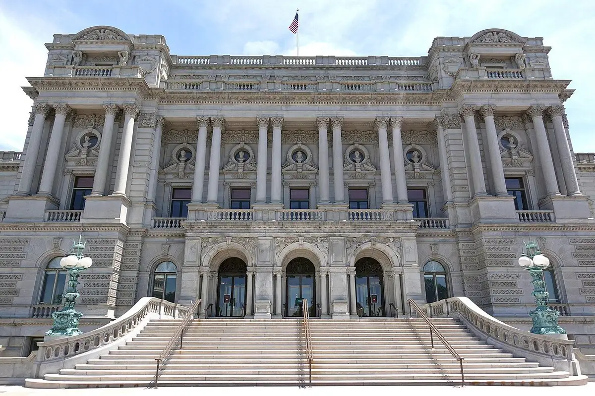 The front of the Library of Congress Jefferson Building, with its wide staircase, rows of columns and bronze lamp posts under an early-summer blue sky.