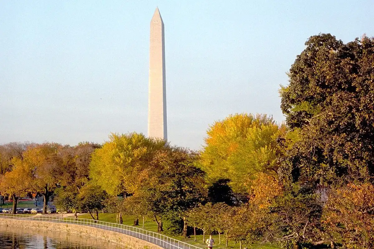 The Washington Monument rising beyond autumn trees and calm water.