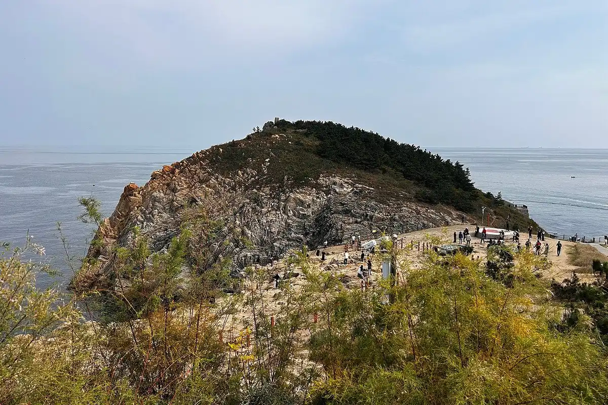 A rocky headland and footpath reaching into the sea at Weihai in autumn light.