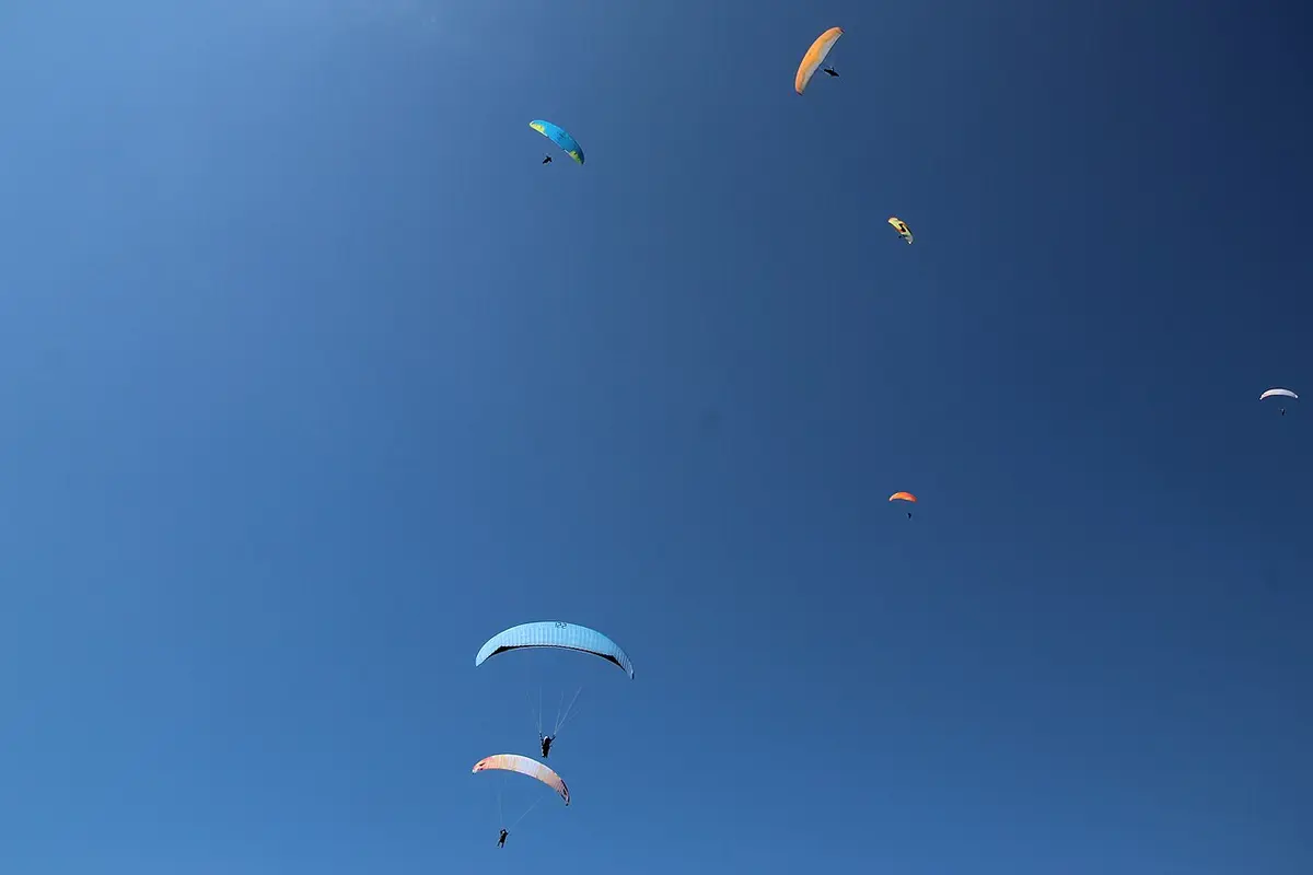 山と湖の上空を飛ぶ何機ものパラグライダー。
