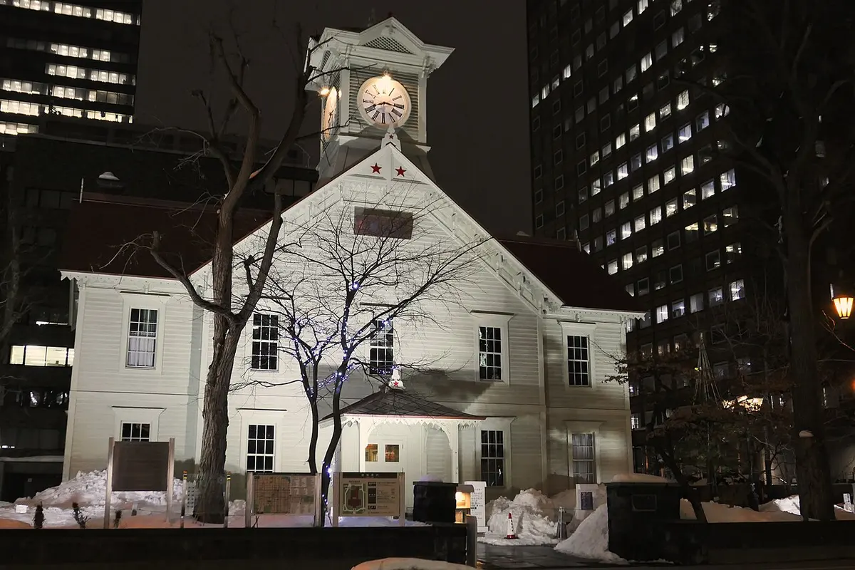 A quiet, snow-covered street in front of the Sapporo Clock Tower at night.